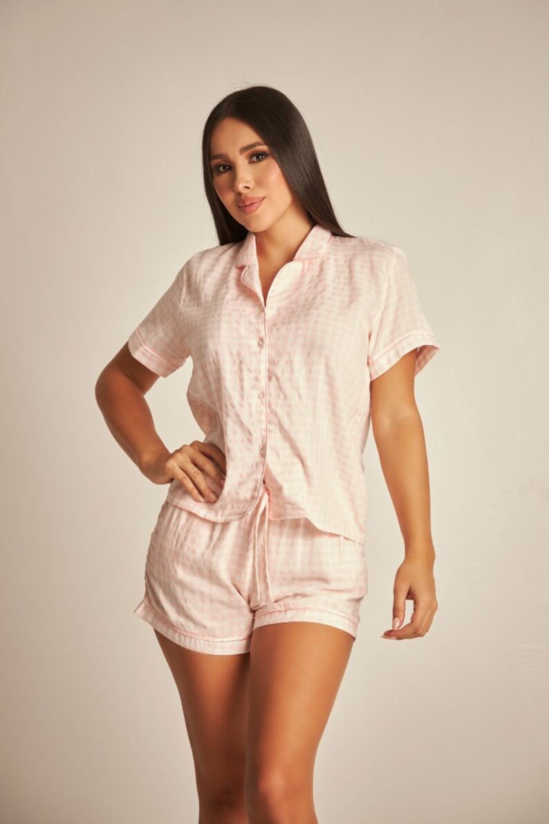 May include: A pink and white gingham pyjama set with a short-sleeved button-up top and matching shorts.