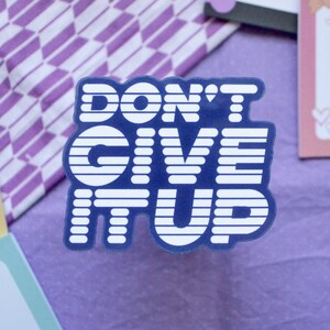 May include: Blue and white sticker with the text "DON'T GIVE IT UP" in a retro style font.