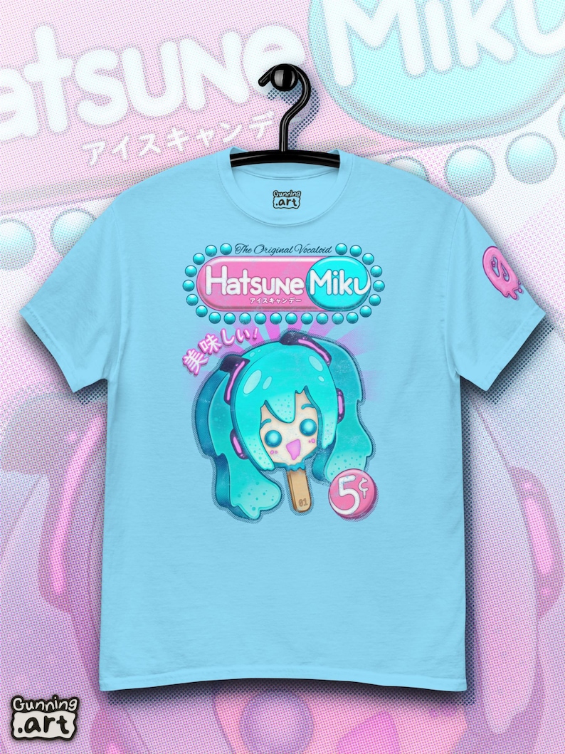Op de afbeelding: Lichtblauw T-shirt met een afbeelding van Hatsune Miku als ijslolly. Het ontwerp bevat de tekst "Hatsune Miku" en Japanse tekst. Het shirt hangt aan een zwarte hanger.