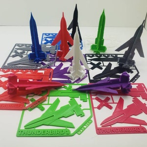 Puede incluir: Un conjunto de 10 kits de modelos impresos en 3D de la icónica nave espacial Thunderbird de la clásica serie de televisión. Cada kit es de un color diferente, incluyendo rojo, verde, azul, blanco, negro y morado. Los kits están etiquetados con el número Thunderbird y la palabra "MAYORE" en la base.