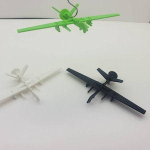 May include: Three small model airplanes in different colors: green, white, and black. The green airplane is suspended from a wire. The other two are on a white surface. Each plane has wings and a tail.