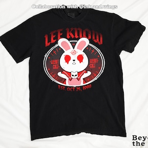May include: Black t-shirt featuring a white rabbit with red eyes and a red cape, surrounded by a circular design with the text "LEE KNOW" and "LEEMT CULT". The shirt also includes the text "EST. OCT 25, 1998".