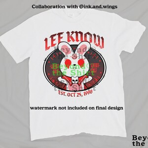 May include: White t-shirt featuring a cartoon rabbit with red eyes and a red cape, encircled by a black oval with the text "LEE KNOW" in red. The shirt also includes the text "EST. OCT 25, 1998" and "Beyond the Shirt".
