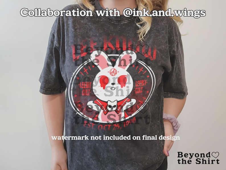 May include: Dark gray t-shirt featuring a white rabbit with red eyes and a cat graphic. The shirt has the text "Be Kind" and "LeeBit Shi" in red. The shirt also has the text "EST OCT 25, 1998".