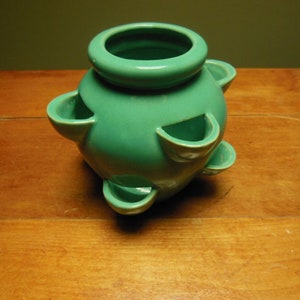 May include: A teal ceramic planter with six small openings around the sides for planting herbs or small plants.