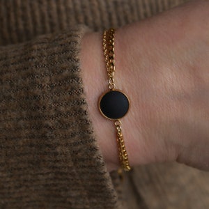 May include: A gold chain bracelet with a black circular pendant.