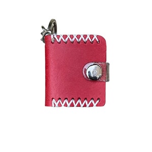 May include: A small red leather keychain with a white stitched border and a clear plastic button closure.