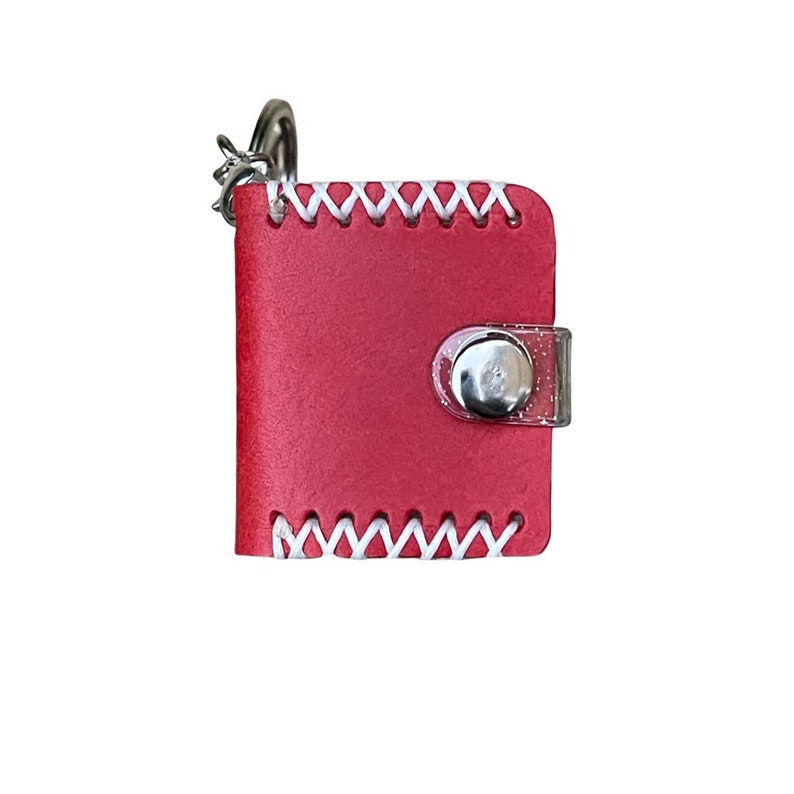 May include: A small red leather keychain with a white stitched border and a clear plastic button closure.