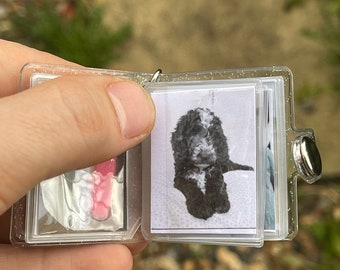 May include: A clear plastic photo album with a silver clasp. The album is open to reveal a black and white photo of a small dog.