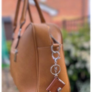 May include: A brown leather handbag with a silver key chain and a small brown leather pouch attached.