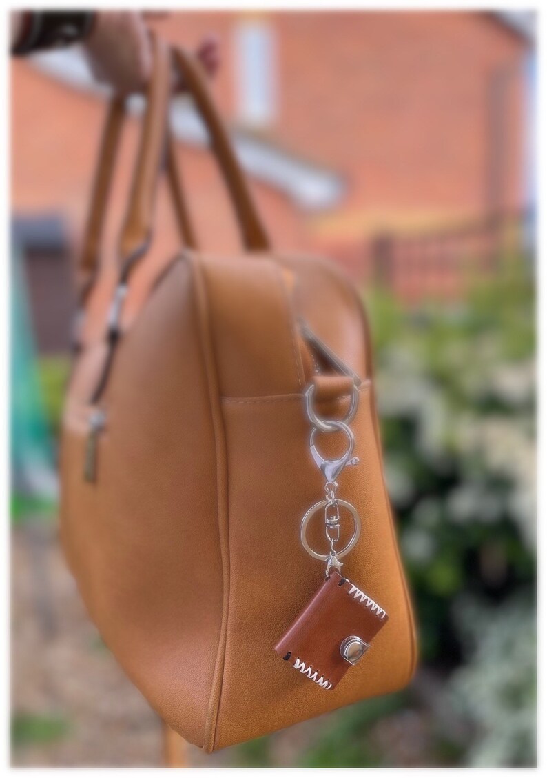 May include: A brown leather handbag with a silver key chain and a small brown leather pouch attached.