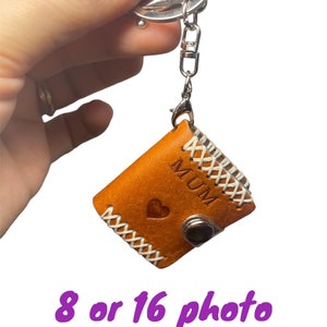 May include: A brown leather photo album keychain with a white stitched border. The album has a heart and the word "MUM" embossed on the front. The keychain is attached to a silver metal ring.