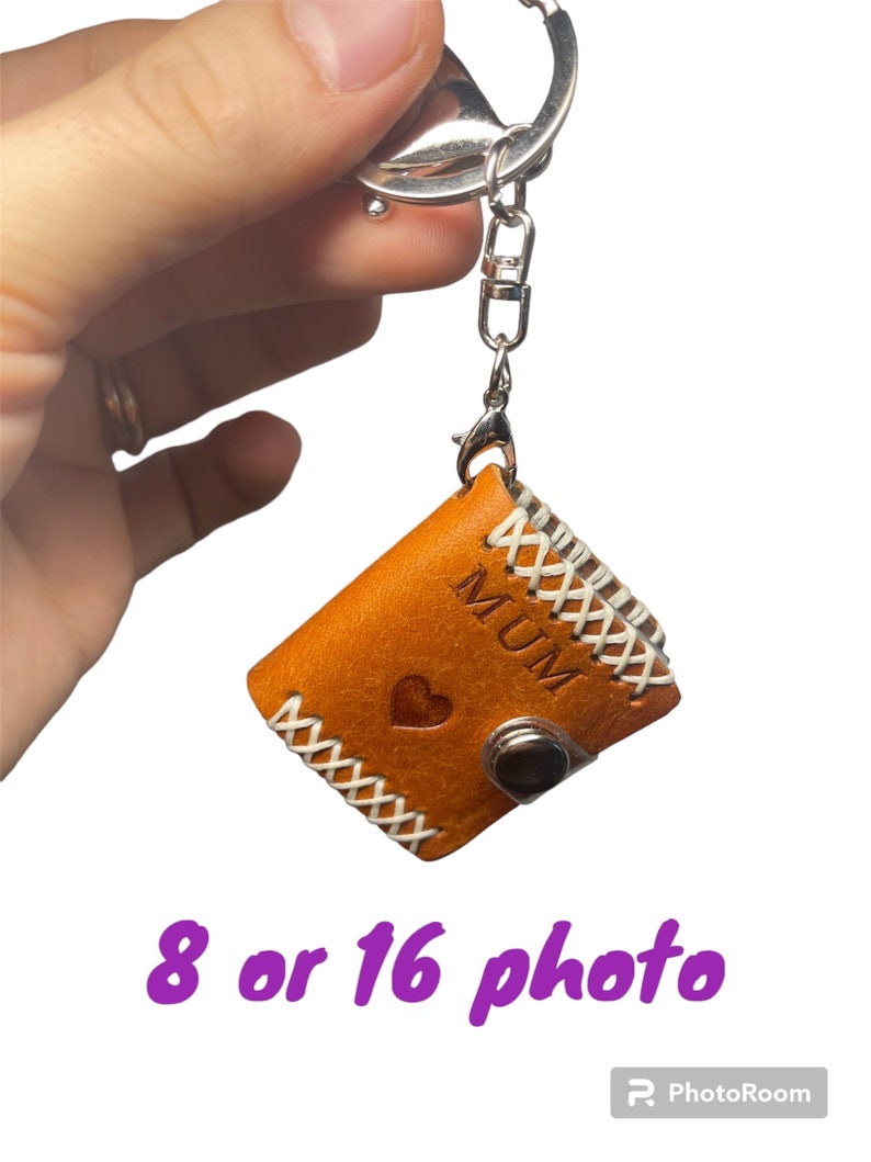 May include: A brown leather photo album keychain with a white stitched border. The album has a heart and the word "MUM" embossed on the front. The keychain is attached to a silver metal ring.