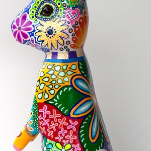 May include: A colorful, hand-painted ceramic rabbit figurine with a green, yellow, blue, red, and pink floral pattern. The rabbit has a long, pointed nose and large, round ears.