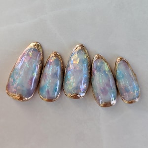 Puede incluir: Cinco puntas de u&ntilde;as ovaladas iridiscentes con un borde met&aacute;lico dorado. Las u&ntilde;as tienen un efecto nacarado y opalescente con tonos de azul, morado y rosa. El borde dorado a&ntilde;ade un toque de elegancia al arte de u&ntilde;as.