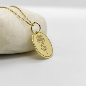 May include: A gold necklace with a delicate chain and a pendant featuring a floral design. The pendant is oval-shaped and has a smooth, polished finish.