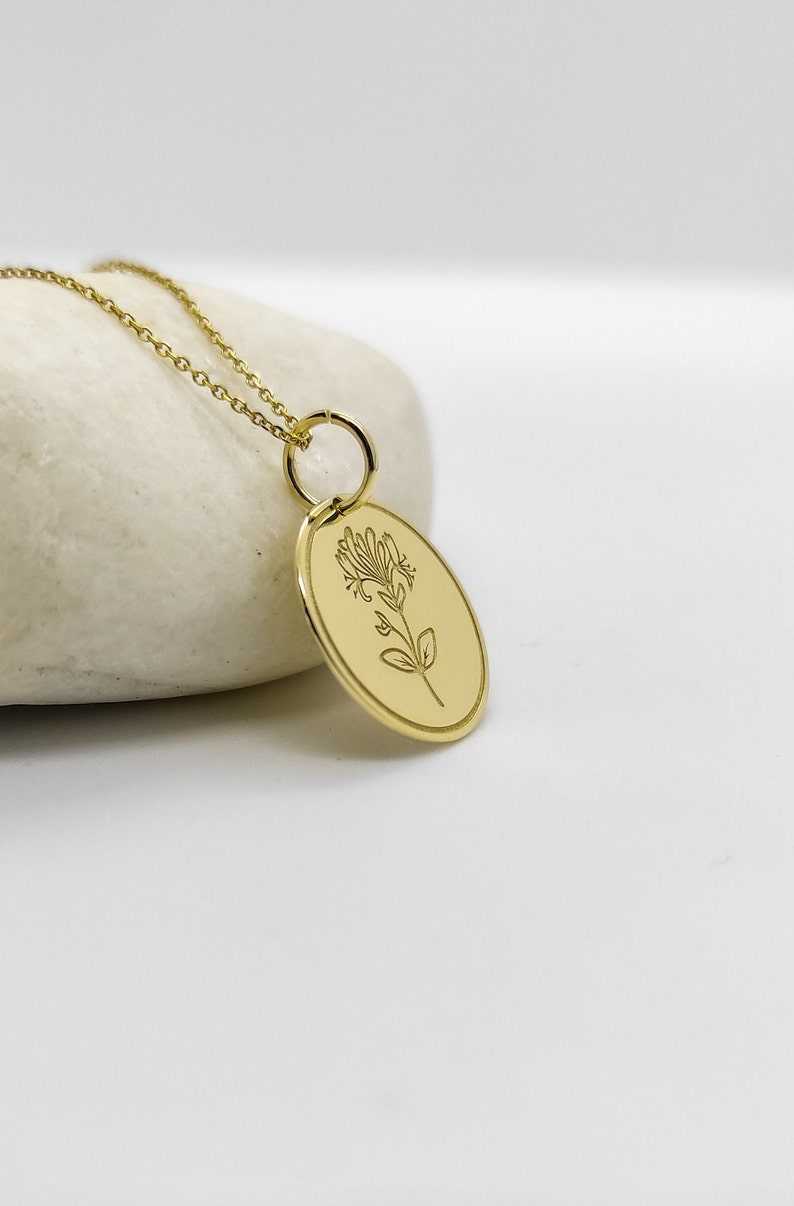 May include: A gold necklace with a delicate chain and a pendant featuring a floral design. The pendant is oval-shaped and has a smooth, polished finish.