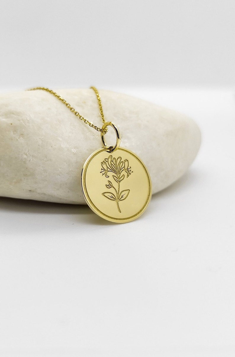 May include: A gold necklace with a round pendant featuring a delicate floral design. The pendant is engraved with a stylized flower.