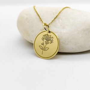 May include: A gold necklace with a round pendant featuring a delicate floral design. The pendant is engraved with a stylized flower.