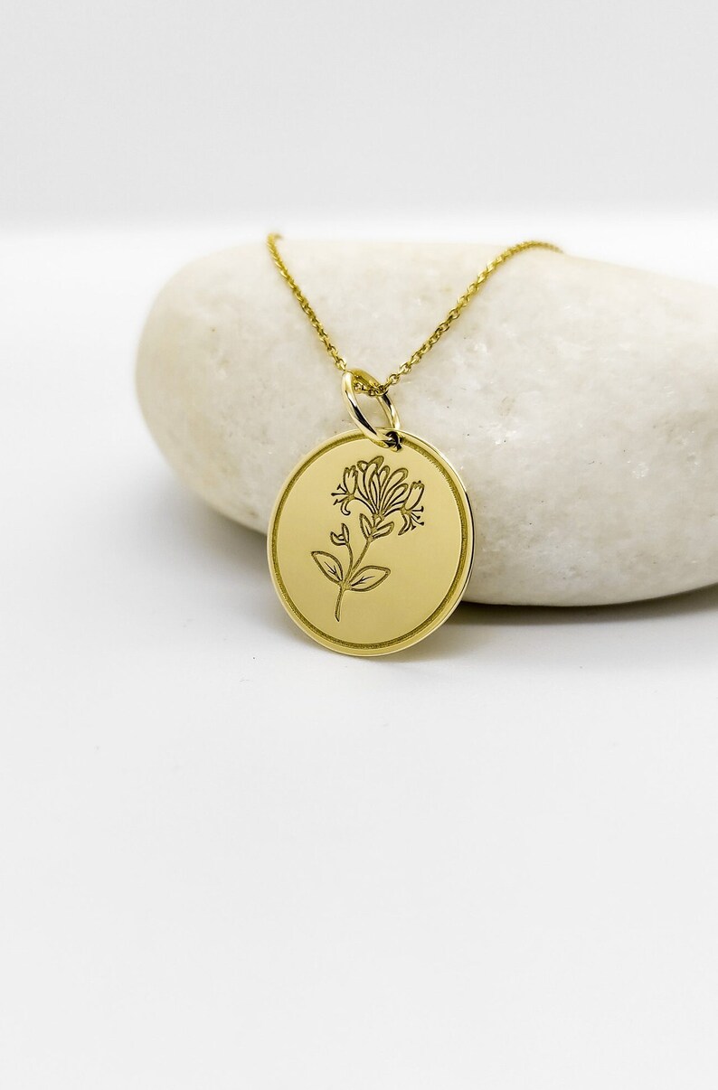 May include: A gold necklace with a round pendant featuring a delicate floral design. The pendant is engraved with a stylized flower.