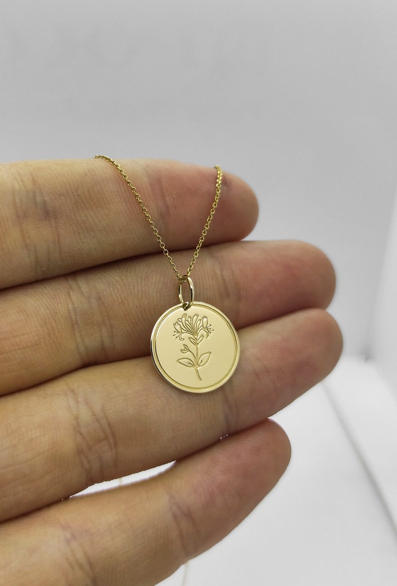 May include: A gold necklace with a round pendant featuring a delicate engraved floral design.