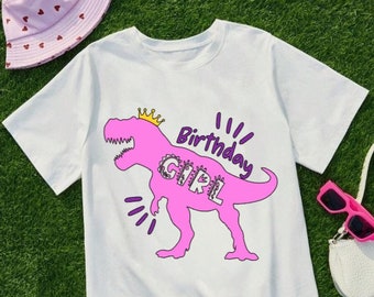 May include: White t-shirt with a pink dinosaur wearing a crown and the words "Birthday Girl" printed on it.
