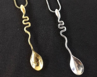 May include: Two necklaces with a spoon pendant. One necklace has a gold chain and a gold spoon pendant. The other necklace has a silver chain and a silver spoon pendant. Both spoons are twisted into a wavy shape.