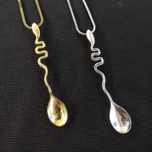 Op de afbeelding: Twee kettingen met een lepel hanger. De ene ketting heeft een gouden ketting en een gouden lepel hanger. De andere ketting heeft een zilveren ketting en een zilveren lepel hanger. Beide lepels zijn gedraaid in een golvende vorm.