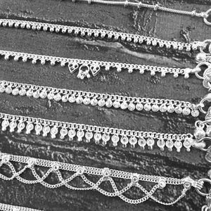 Pode incluir: Uma cole&ccedil;&atilde;o de pulseiras de tornozelo prateadas em v&aacute;rios designs. As pulseiras de tornozelo apresentam correntes delicadas, detalhes de contas e pingentes decorativos. A imagem &eacute; em preto e branco, destacando os detalhes intrincados das joias.