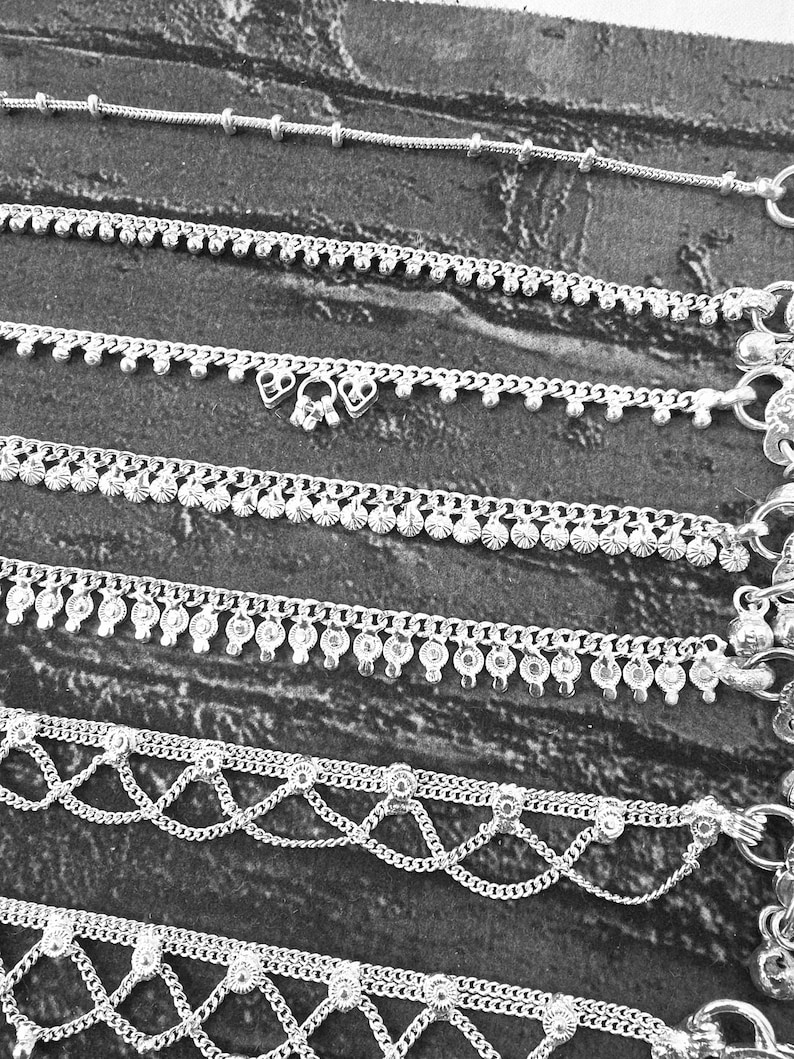 Pode incluir: Uma cole&ccedil;&atilde;o de pulseiras de tornozelo prateadas em v&aacute;rios designs. As pulseiras de tornozelo apresentam correntes delicadas, detalhes de contas e pingentes decorativos. A imagem &eacute; em preto e branco, destacando os detalhes intrincados das joias.