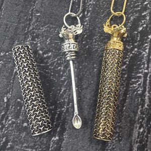 Puede incluir: Tres colgantes metálicos y recipientes cilíndricos a juego. Un colgante es plateado con un diseño de cabeza de ciervo y una cuchara pequeña. El segundo colgante es dorado con un diseño de cabeza de ciervo y un recipiente cilíndrico. El tercero es plateado.