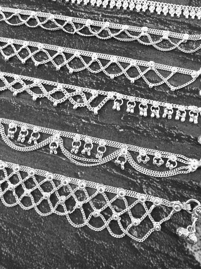Pode incluir: Close-up de v&aacute;rias tornozeleiras prateadas com designs intrincados. As tornozeleiras apresentam correntes delicadas, detalhes de contas e pingentes pendurados. Os designs incluem padr&otilde;es geom&eacute;tricos e bordas onduladas.