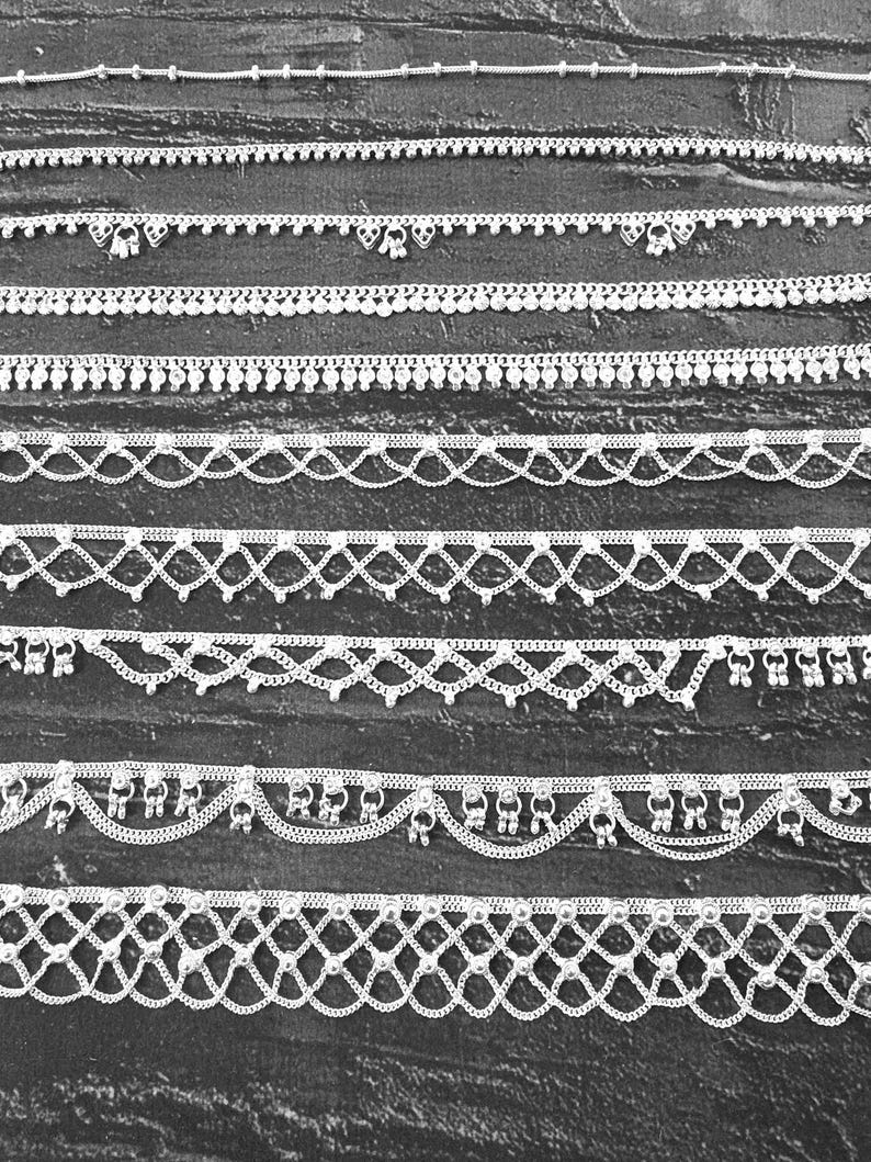 Pode incluir: Uma cole&ccedil;&atilde;o de pulseiras de tornozelo prateadas com v&aacute;rios designs. As pulseiras de tornozelo apresentam correntes delicadas, detalhes de contas e pingentes pendurados. As pulseiras de tornozelo s&atilde;o exibidas em um fundo escuro, mostrando seus detalhes intrincados e superf&iacute;cies reflexivas.