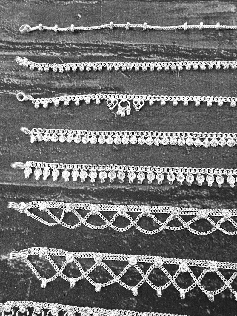 Pode incluir: Uma cole&ccedil;&atilde;o de pulseiras de tornozelo prateadas com v&aacute;rios designs. As pulseiras de tornozelo apresentam correntes delicadas, contas e pingentes decorativos. Algumas t&ecirc;m padr&otilde;es intrincados, enquanto outras s&atilde;o simples e elegantes. As pulseiras de tornozelo s&atilde;o exibidas em uma superf&iacute;cie escura e texturizada.