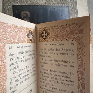 Pu&ograve; includere: Libro d'epoca aperto con pagine con bordi decorativi rosa e oro. Il testo &egrave; in spagnolo, con i numeri di pagina 58 e 59 visibili. Un piccolo segnalibro &egrave; attaccato.