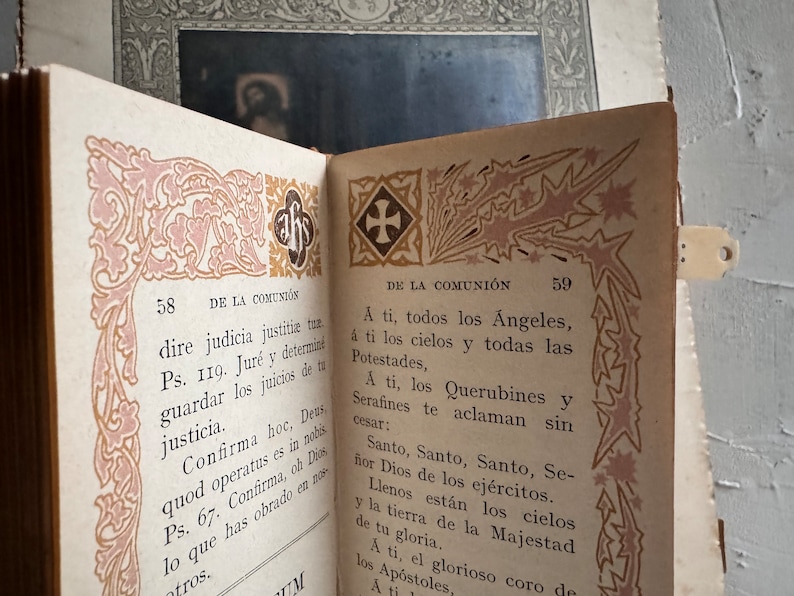 Pu&ograve; includere: Libro d'epoca aperto con pagine con bordi decorativi rosa e oro. Il testo &egrave; in spagnolo, con i numeri di pagina 58 e 59 visibili. Un piccolo segnalibro &egrave; attaccato.