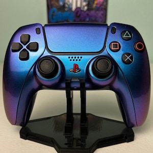 May include: A purple and blue iridescent PlayStation 5 DualSense controller on a black stand. The controller has a black PlayStation logo on the front.