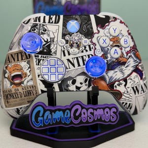 May include: A custom Xbox controller featuring a black and white collage of One Piece wanted posters, including Monkey D. Luffy. The controller has translucent blue thumbsticks, white action buttons, and a central logo button with a skull icon.