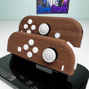 May include: Two wooden Nintendo Switch controllers with white buttons and a black stand. The controllers have a wood grain pattern and the stand has the Nintendo Switch logo.