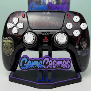 May include: A black wireless video game controller featuring Resident Evil branding, a Raccoon City police badge graphic, and a character illustration. The controller has silver buttons, joysticks, and a glossy finish with red blood-like splatter accents.