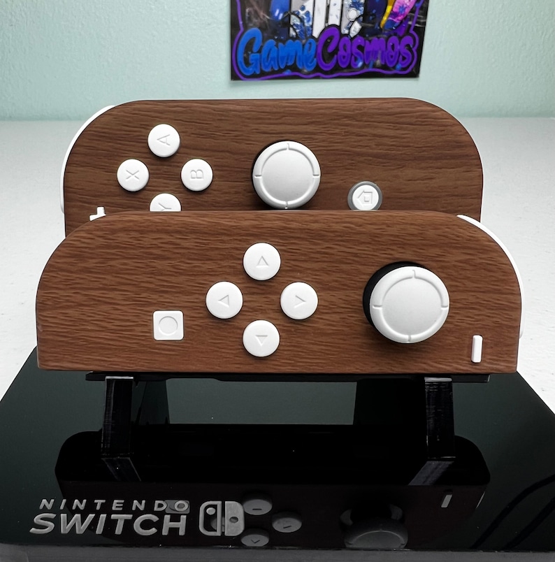 May include: A wooden Nintendo Switch controller stand with a brown woodgrain finish. The stand has two controllers, one on top of the other, with white buttons and a white joystick.