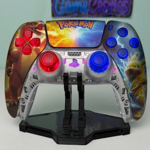 May include: A custom video game controller featuring a clear shell with internal LED lighting. The left side displays Charizard, the right side shows Pikachu, and the centre touchpad features the Pokémon logo with a bright light effect.