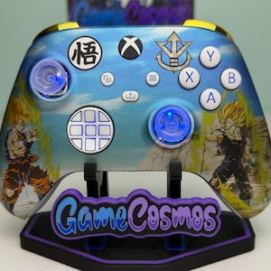 May include: A custom Xbox wireless controller featuring a blue sky gradient finish with Dragon Ball Z character graphics. The controller includes white action buttons, a D-pad with a grid pattern, and two analogue sticks with glowing blue LED rings.
