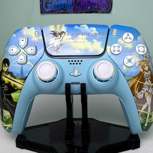 Könnte beinhalten: Ein blauer PlayStation 5 DualSense-Controller mit einer benutzerdefinierten Haut, die Charaktere aus dem Anime Sword Art Online zeigt. Der Controller hat ein blaues und weißes Farbschema und zeigt den japanischen Text "ソードアート・オンライン" (Sword Art Online) und "アリシゼーション" (Alicization).