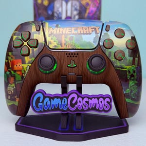 以下が含まれることがあります： Minecraftをテーマにしたカスタムビデオゲームコントローラー。 コントローラーは木目調のデザインで、緑色のアクセントとMinecraftのグラフィックが施されています。 コントローラーは「Game Cosmos」の文字が入った黒いスタンドに置かれています。