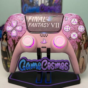May include: Pink Final Fantasy VII custom game controller with cherry blossom design and character art. The controller has a matching stand with the text "Game Cosmos". The buttons and joysticks have a purple glow.