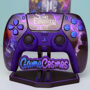 Puede incluir: Un mando de videojuegos personalizado morado y negro con el texto "Solo Leveling ARISE". El mando tiene botones azules y un soporte a juego con el texto "Game Cosmos".