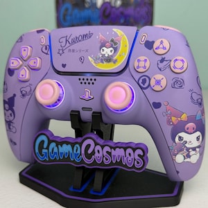 Op de afbeelding: Een paarse draadloze videogamecontroller met Kuromi-karakterafbeeldingen, een gele maansikkel en de tekst Kuromi en Game Cosmos. De controller heeft lichtroze thumbsticks, lichtroze knoppen en geïntegreerde paarse ledverlichting.