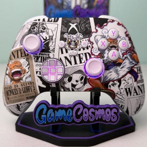 May include: Custom Xbox controller featuring a black and white manga-style design with characters and the word "WANTED." The controller has pink and white buttons, and a matching stand with the text "Game Cosmos."