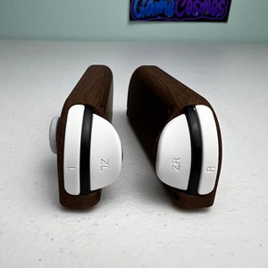 May include: Two wooden controller grips for the Nintendo Switch. The grips are brown and have white buttons labeled "ZL" and "ZR" on the left and right grips, respectively.